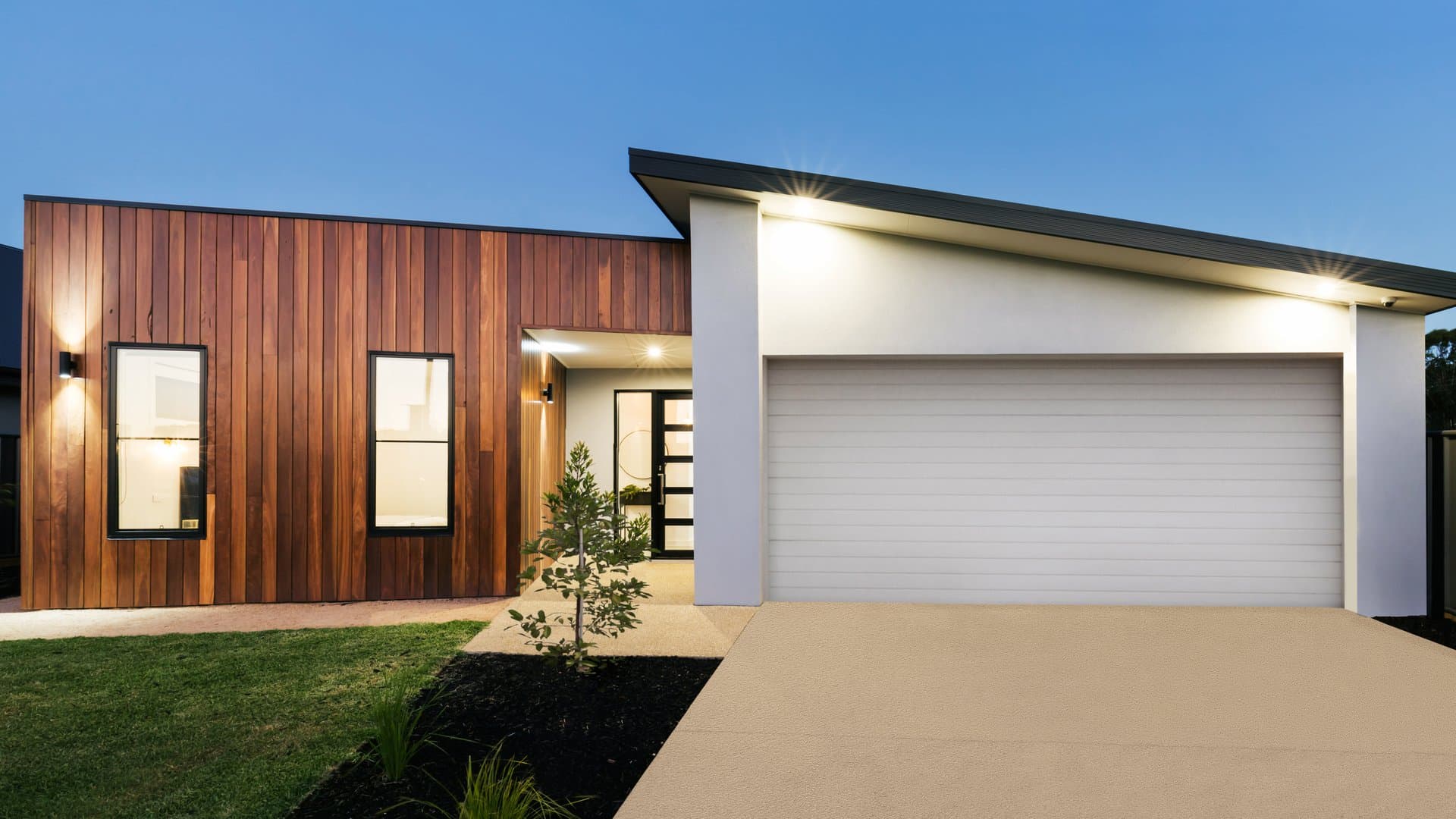 New home exterior with wall lights and garage downlights at dusk